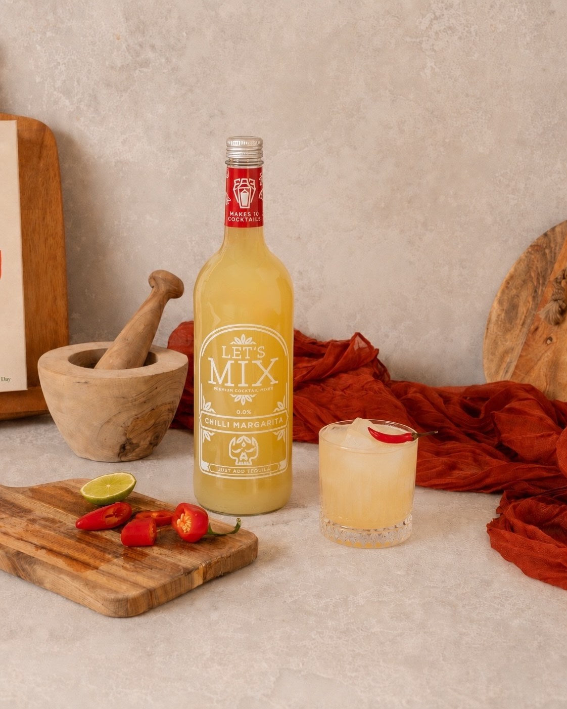 Salt-rimmed Chilli Margarita with fresh chillies and lime next to a bottle of Let's Mix Chilli Margarita Mix